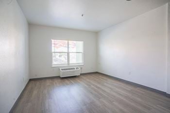 The living room of an empty house with wooden floors and a window